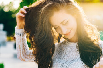 Headshot of a young trendy brunette standing outdoors and adjusting her hair on a sunny summer day.