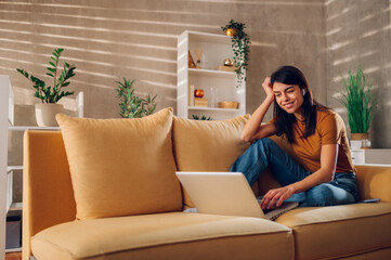 Woman using laptop while sitting on a yellow sofa at home