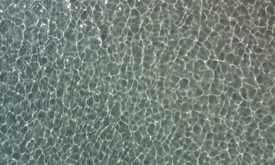 Top view of transparent water sea with stone and pebbles bottom. Sun glare on the surface crystal...