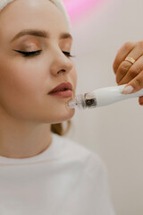 A beautiful young girl in a beauty salon on a facial rejuvenation procedure smiles while a master cosmetologist makes her skin lifting close-up