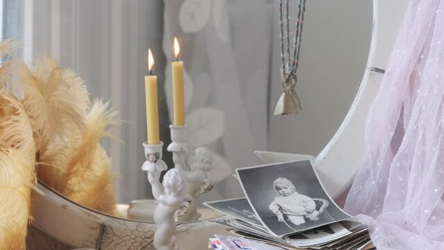 female hands holds old photographs, porcelain figurine, candlestick cupid with golden wings, angel miniature, candle burning front mirror, nostalgia and memories, home archive, family tree, genealogy