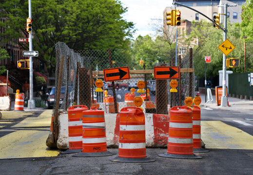 road work on a city street intersection (orange cones, bollards, barricades) arrows traffic light and trees construction infrastructure transportation