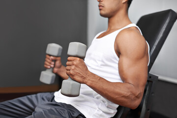 Fototapeta na wymiar Building bulging biceps. Side view of a muscular man lifting dumbbells.