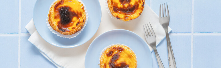 Traditional Portuguese egg tarts dessert Pasteis Pastel de nata or Pastels de Belem with forks on the blue tile. Flat lay