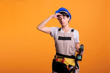 Tired young contractor with drilling gun feeling sleepy and fatigued, falling asleep at renovating project work. Female builder being exhausted with burnout and holding drill screw tool.