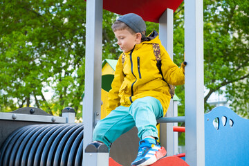 Portrait of six year old boy in yellow jacket playing on playground..