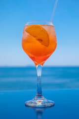 A glass of Aperol spritz cocktail on the background of the blue sea and sky.