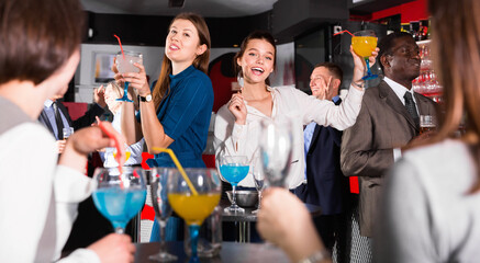 Young glad positive attractive women with cocktails having fun with workmates on office party at nightclub