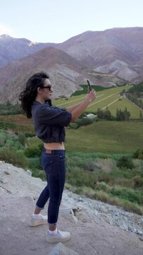 joven mujer latina de perfil grabando o tomando fotos con su celular al paisaje al atardecer en el Valle del Elqui Provincia de Paihuano