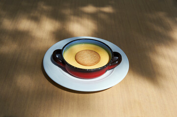 custard with round biscuit in red metal pan on white plate