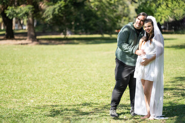 Fototapeta premium Pregnant woman in wedding dress posing with her partner outdoors