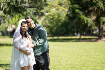 Fototapeta premium Pregnant woman in wedding dress posing with her partner outdoors