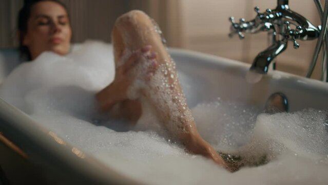 Carefree lady washing legs in foam bath closeup. Sexy woman touching body skin