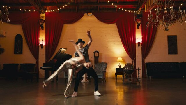 Impressive flips with twine or cartwheel performed by young asian woman supported by partner. Slow motion pair of dancers training in retro style interior with chandeliers cinematic RED camera shot 4K