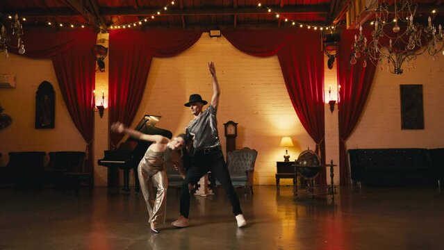 Slow motion glamorous girl acrobat performs flips with twine, doing cartwheel supported by dance partner. Dancers training in retro style vintage interior with chandeliers cinematic shot on RED camera