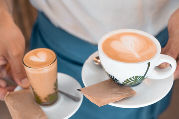 Waiter serving two different art latte coffees; a cortado coffee and a milk coffee in a cafeteria.