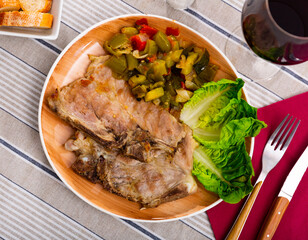 Juicy roast pork on a plate with a side dish of stewed vegetables, garnished with fresh lettuce leaves