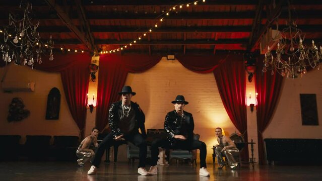 Glamorous group of people wearing fashionable glittery elegant black golden costumes having fun indoors, dancing in pairs and going sexy dance moves, jumping, spinning, high kicking legs or battement
