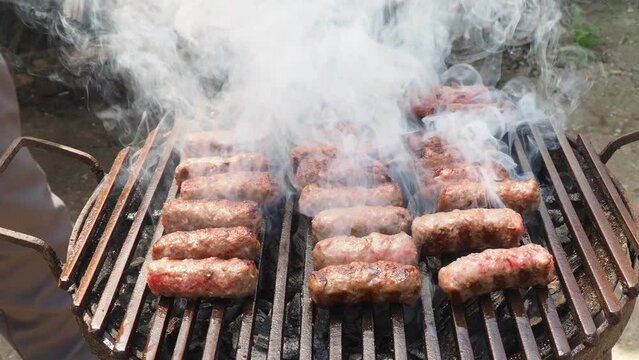 Crackling. Roasting chevaps on a grill grate. Lots of white smoke. Cevapi, cevapcici is a grilled dish minced meat found traditionally in the countries of southeast Europe and Balkans. Turkish kebap.