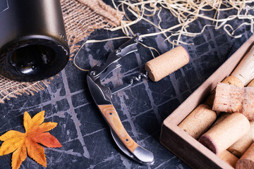 Corkscrew and dusty wine bottle close-up. An open bottle on an old black table.