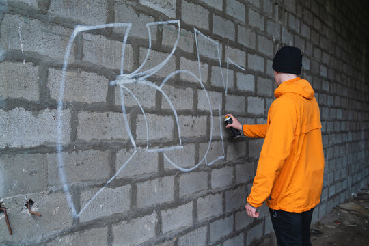One young guy drawing graffiti on wall with spray can and mask on his face during the day