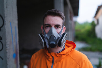 One young guy drawing graffiti on wall with spray can and mask on his face during the day