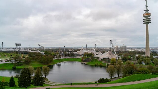 Captivating timelapse of the Olympiapark in Munich, Germany during autumn featuring a cloudy sky, high tower, lake, and stunning skyline.