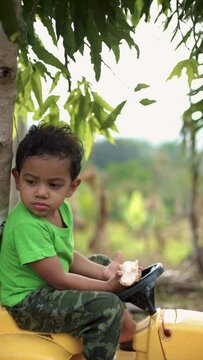 boy sitting in a toy car eating guaba