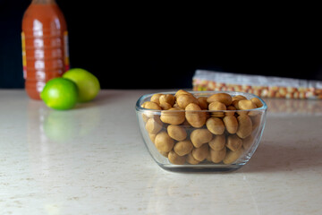 Cacahuates japoneses en tazón con salsa picante y limones al fondo. 