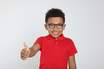 African-American boy with glasses showing thumb up on light grey background