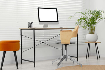 Stylish office interior with comfortable chair, desk, computer and houseplant