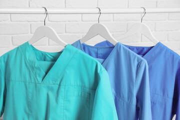 Medical uniforms hanging on rack near white brick wall, closeup