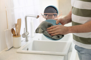 Man wiping plate with towel above sink in kitchen, closeup