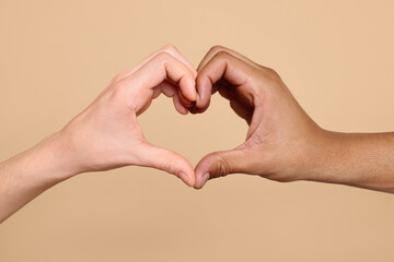 International relationships. People making heart with hands on light brown background, closeup