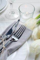 Stylish setting with cutlery, burning candle and tulips on white wooden table, closeup