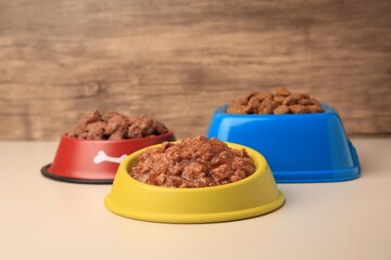 Dry and wet pet food in feeding bowls on beige background