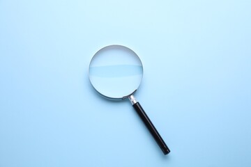 Magnifying glass on light blue background, top view