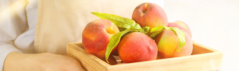 Woman holding wooden crate with fresh ripe peaches, closeup. Banner design