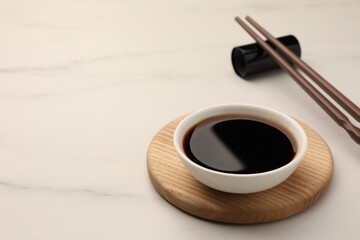 Bowl with soy sauce and chopsticks on white marble table. Space for text