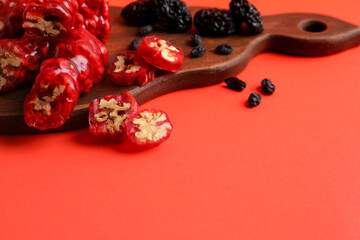 Wooden board with tasty churchkhela, raisin and prunes on color background