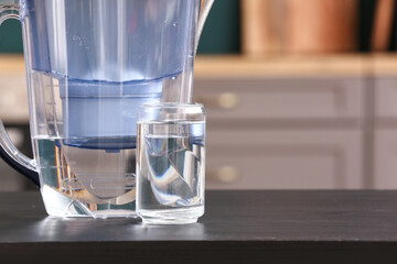 Modern filter jug and glass of water on black table in kitchen