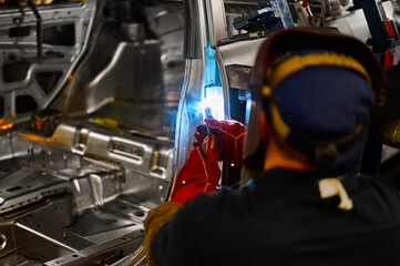 Welder in helmet works with metal parts of car carcass