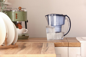 Glass of pure water and filter jug on wooden kitchen counter