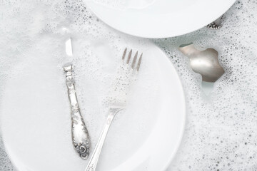 Plates with cutlery and foam in water, closeup