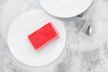Cleaning sponge with dishes and foam in water, closeup
