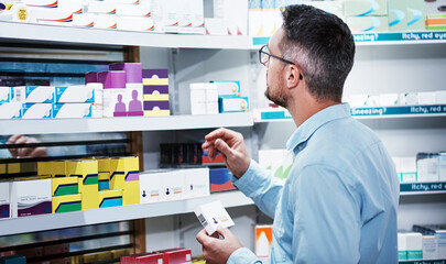 Naklejka na ściany i meble Comparing products to make the best choice. a mature man looking at products in a pharmacy.