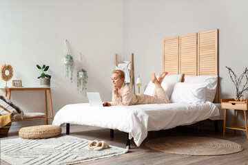 Young woman using laptop on bed in morning
