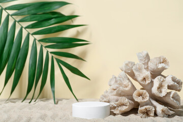 Fototapeta na wymiar Decorative plaster podium, coral and palm leaves in sand on light background