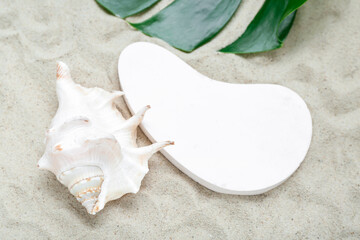 Fototapeta na wymiar Decorative plaster podium, seashell and tropical leaf in sand, closeup