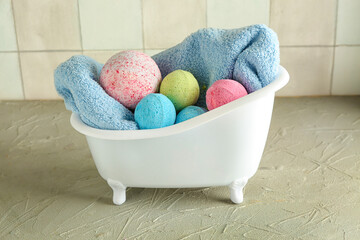 Little bathtub with bath bombs and towel on table near tile wall